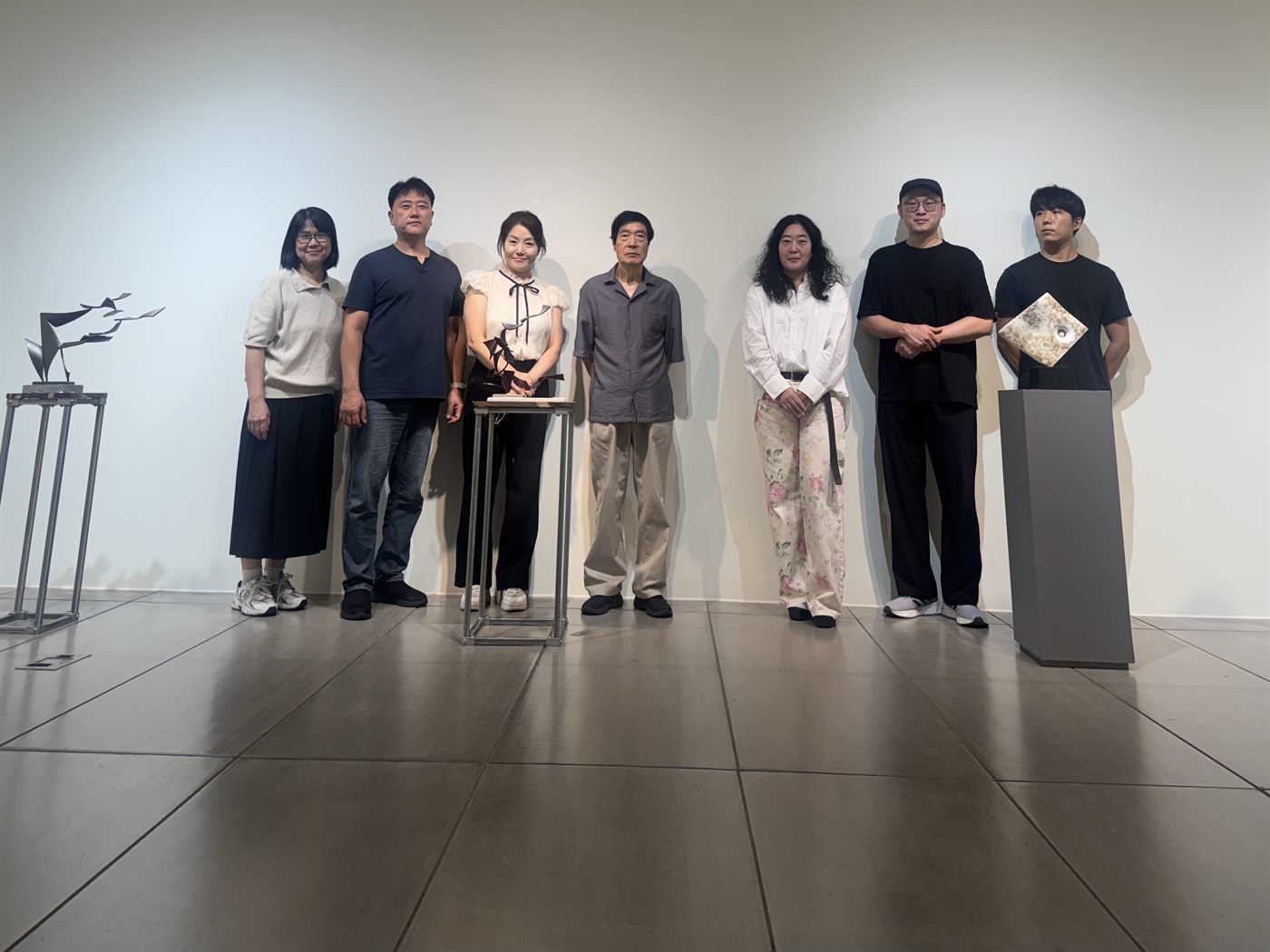 2026 경남조각가협회전 참여작가 단체사진 — 작품 좌대 사이에 나란히 선 작가들